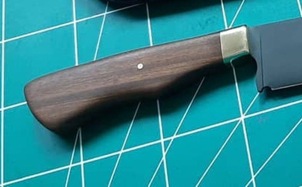 Detalhe do cabo de imbuia em faca artesanal Runefall com acabamento em metal e pino de fixação