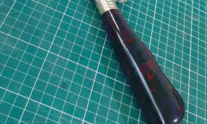 Cabo de faca artesanal em Micarta com padrão marmorizado vermelho e azul, exemplo de material moderno usado como alternativa à madeira