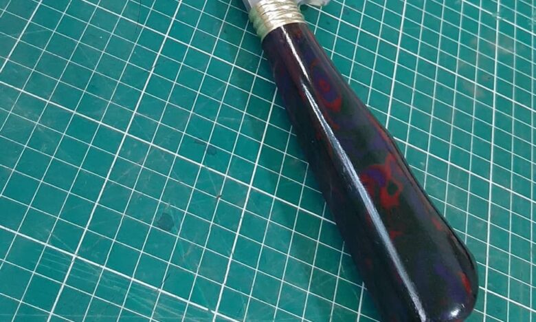 Cabo de faca artesanal em Micarta com padrão marmorizado vermelho e azul, exemplo de material moderno usado como alternativa à madeira