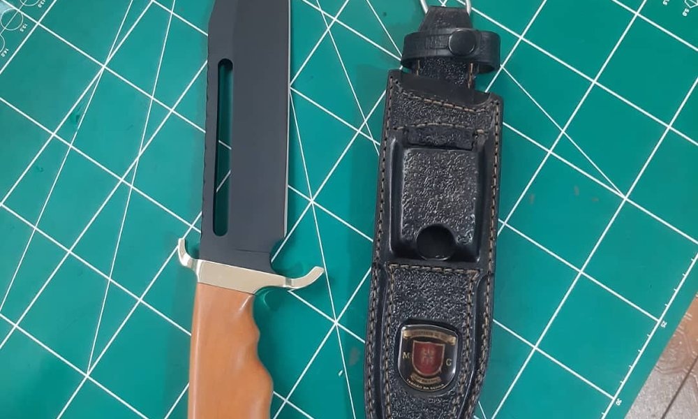 Faca tática estilo militar com guarda em metal dourado e bainha em couro preto com emblema